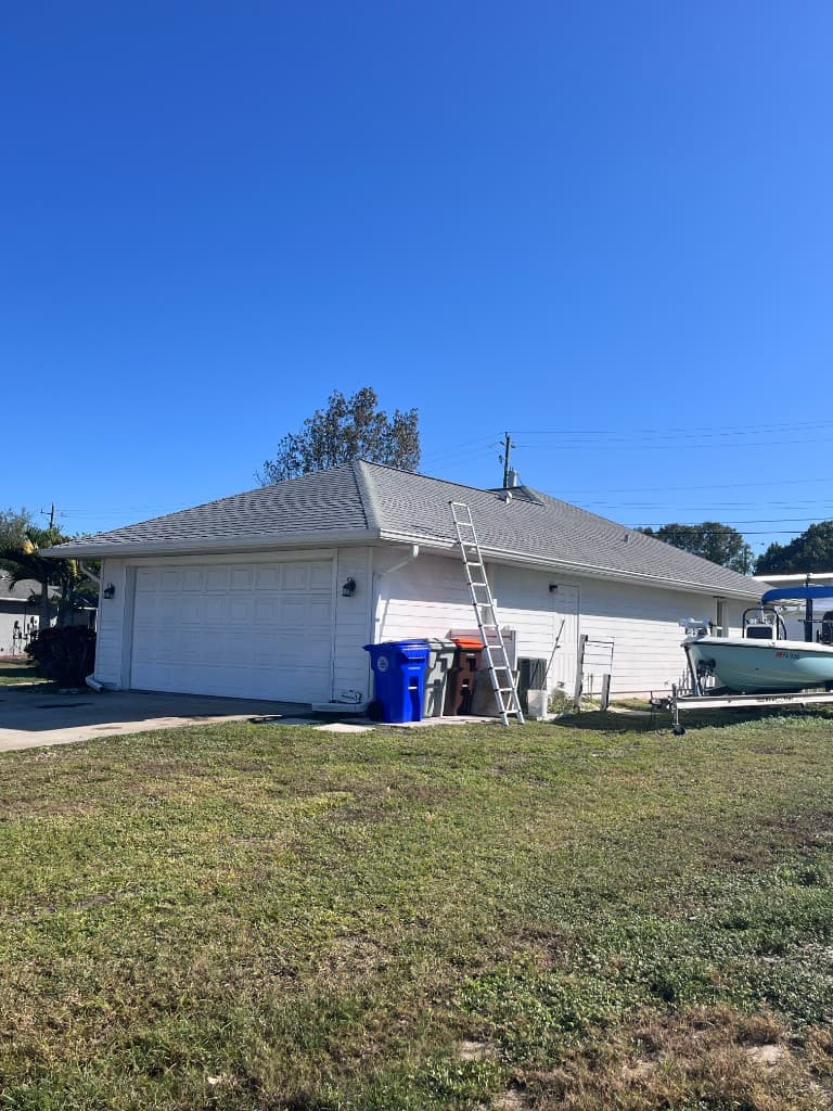 A white hip-roof house with a garage, a ladder at the eave, and a boat in the side yard